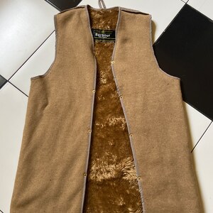 Puede incluir: Un chaleco marrón de la marca Barbour con forro polar. El chaleco tiene cierre de cremallera y cierre de botón.