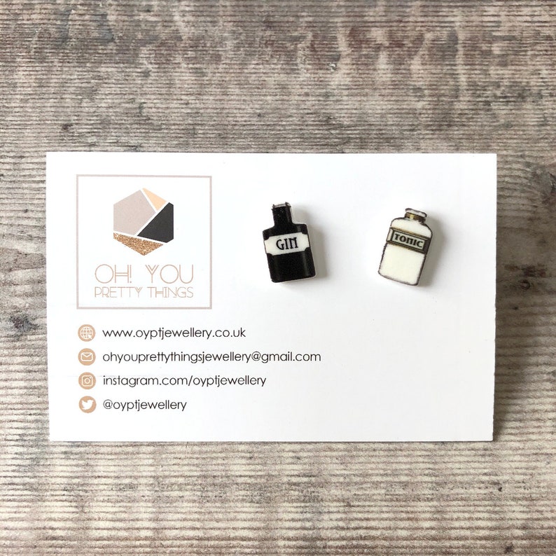 May include: A pair of earrings featuring miniature black and white bottles with the words "GIN" and "TONIC" printed on them.