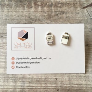 May include: A pair of white and gold earrings shaped like miniature bottles. One bottle says "Gin" and the other says "Tonic".