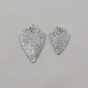 May include: Two silver arrowhead pendants with a textured surface. The larger pendant is about 2 inches long and the smaller pendant is about 1 inch long.