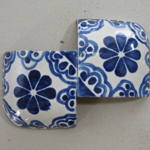 May include: Two white ceramic tiles with a blue floral pattern. The tiles are joined together to form a corner piece.