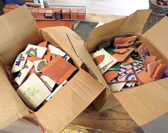 May include: Two cardboard boxes filled with broken colorful ceramic tiles. The tiles have floral and geometric patterns in shades of blue, green, yellow, and orange.