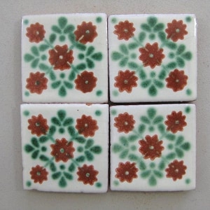 May include: Four square ceramic tiles with a white background and a repeating pattern of red flowers and green leaves.