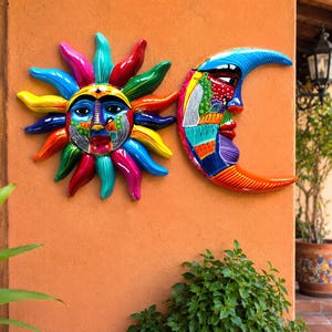 May include: A pair of ceramic wall plaques featuring a sun and a crescent moon. The sun has multi-colored rays in red, blue, yellow, and green with a painted face. The crescent moon features a face with blue, red, and green patterned sections.