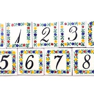 May include: Set of ten ceramic tiles with a floral border and black numbers 0 through 9. The tiles are white with a yellow, red, blue, and green floral border.