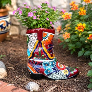 May include: A ceramic cowboy boot planter featuring a vibrant, multi-colored hand-painted floral and geometric pattern in shades of red, blue, yellow, and orange, currently holding a small green plant with tiny pink flowers.
