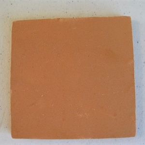 May include: A square terracotta tile with a smooth, slightly textured surface. The tile is a warm, reddish-brown color.