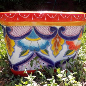 May include: A colorful, hand-painted ceramic planter with a red rim, yellow, blue, and green floral designs, and a white background.