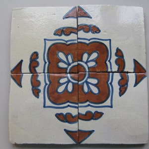 May include: Four square ceramic tiles arranged to form a larger square. Each tile is off-white with a central design in brown, blue, and white. The design features a floral motif with a symmetrical pattern, suitable for home decor.