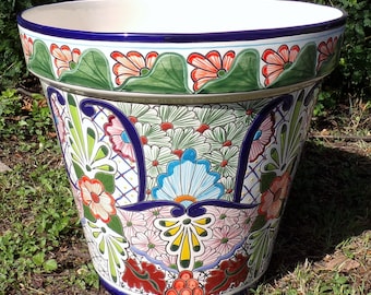 May include: A large, white ceramic planter with a colorful floral design. The planter has a wide rim and a flared base. The design features green leaves, pink, red, blue, and yellow flowers.