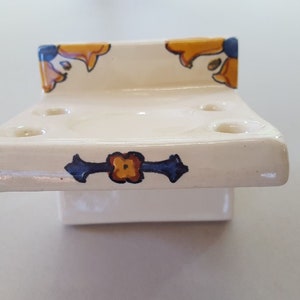 May include: White ceramic toothbrush holder with four holes and a decorative blue and yellow floral design.