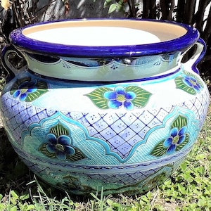 May include: A large, round, blue and white ceramic planter with two handles. The planter is decorated with a floral pattern and a blue and white checkered design.