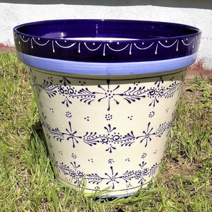 May include: A white ceramic planter with a blue and white floral design. The planter has a wide rim and a rounded base.
