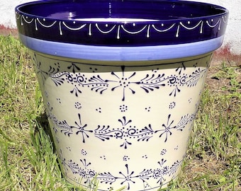 May include: A white ceramic planter with a blue and white floral design. The planter has a wide rim and a rounded base.