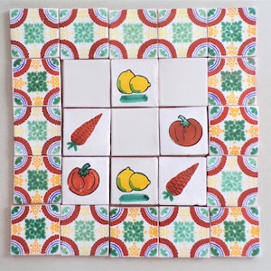 May include: A set of nine white ceramic tiles with a red, green, and yellow border. Each tile features a different painted vegetable or fruit, including carrots, tomatoes, and lemons.