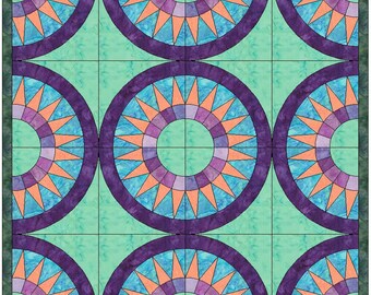 Puede incluir: Un bloque de colcha con un diseño circular que presenta un círculo central rodeado de anillos concéntricos de morado, rosa y naranja. El anillo exterior es de color morado sólido con una fila de triángulos naranjas.