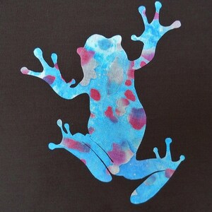 May include: A blue frog silhouette with pink and white watercolor splatter paint on a black background.