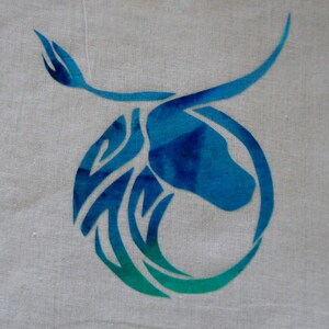 May include: A blue and green stylised bull's head design on a white fabric background.