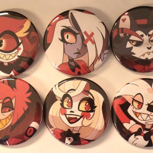 May include: Six round pinback buttons featuring colorful cartoon character illustrations. The buttons showcase various characters with distinct facial expressions and designs, including red, black, and white color schemes. The buttons are arranged in two rows of three.