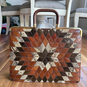 May include: A vintage handbag with a geometric pattern in shades of brown, tan, and black. The bag features a starburst design in the center and a brown handle. The frame is gold-toned.