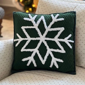 May include: A green throw pillow with a white snowflake design. The snowflake is made of fluffy white fabric and is outlined in white.