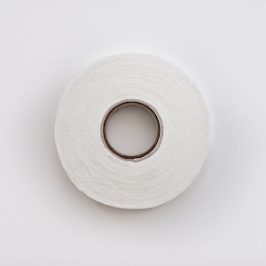 May include: A roll of white athletic tape, wound around a cardboard core. The tape is textured and has a slightly rough surface.