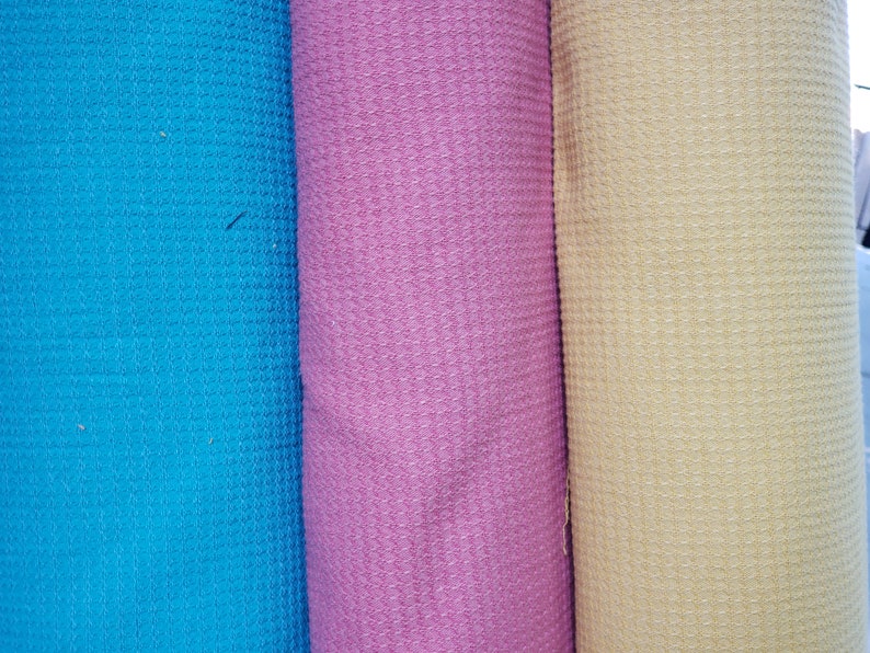 May include: Three rolls of fabric in different colors: blue, pink, and yellow. The fabric has a waffle texture.