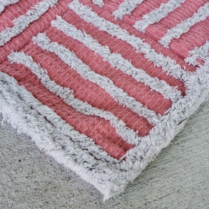 May include: Close-up of a pink and white striped rug with a fuzzy texture. The rug has a geometric pattern and is made of a soft, plush material.