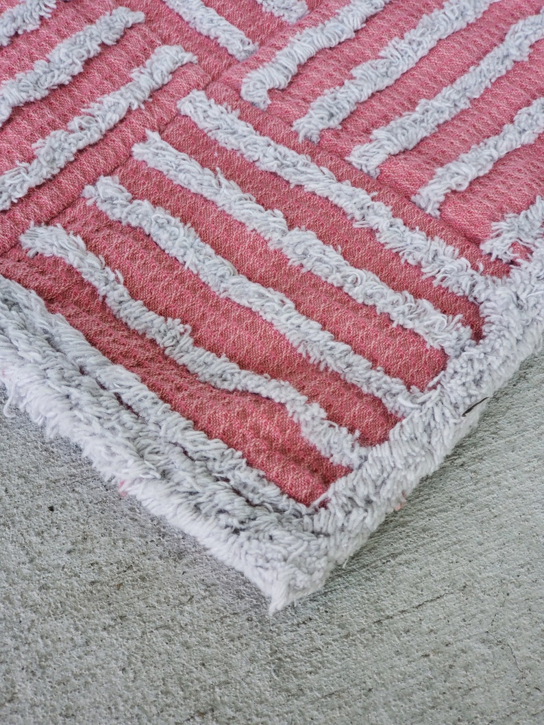 May include: Close-up of a pink and white striped rug with a fuzzy texture. The rug has a geometric pattern and is made of a soft, plush material.