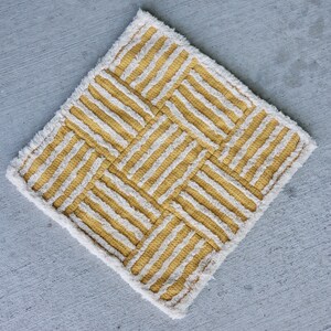 May include: A yellow and white striped rug with a geometric pattern. The rug has a fringe border.
