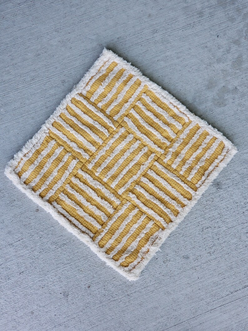 May include: A yellow and white striped rug with a geometric pattern. The rug has a fringe border.