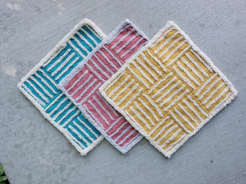 May include: Three bath mats in a woven pattern. The mats are teal, pink, and yellow.
