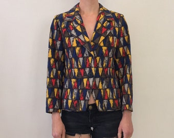 May include: A cropped, fitted blazer with a geometric pattern in shades of blue, red, yellow, and brown. The blazer has a single button closure and a pointed collar.