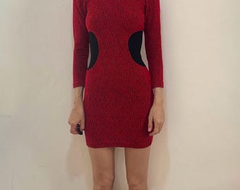 May include: A red textured mini dress with long sleeves and black cutouts on the sides. The dress has a round neckline and a fitted silhouette. The fabric appears to have a subtle pattern. The dress is knee-length.
