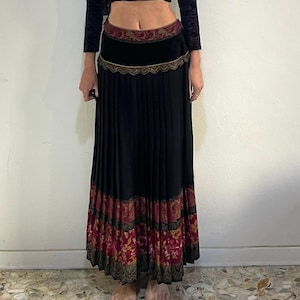 May include: A black velvet wrap top with long sleeves and a pleated black maxi skirt. The skirt features a decorative band at the waist and a patterned border in shades of red, gold, and brown.