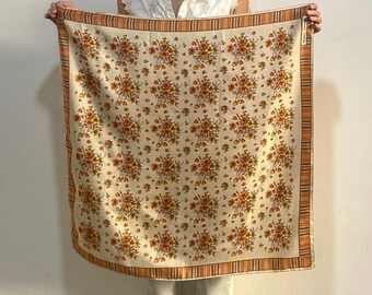 Könnte beinhalten: Ein cremefarbener Seidenschal mit einem floralen Muster in Orange- und Gelbtönen. Der Schal hat einen dünnen orangefarbenen, braunen und weißen Streifenrand.