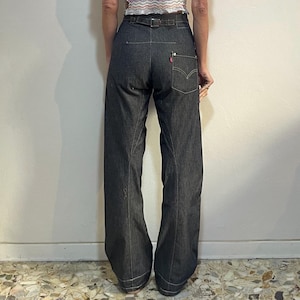 May include: A sheer white blouse with embroidered floral details and puff sleeves is paired with dark wash denim wide-leg pants. The pants have a belt and a red Levi's tag on the back pocket. The pants have a wide leg opening.