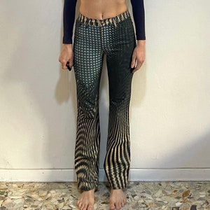 Puede incluir: Un pantal&oacute;n de pierna ancha con estampado negro y verde. El pantal&oacute;n tiene un patr&oacute;n geom&eacute;trico con un dise&ntilde;o ondulado.