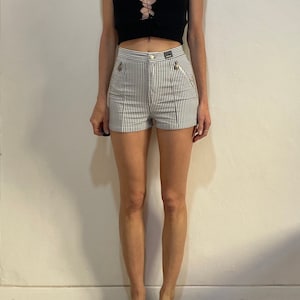May include: A black sleeveless top with a lace-up front is paired with high-waisted shorts. The shorts feature a black and white checkered pattern, a button closure, and small pockets. The outfit is a casual, yet stylish ensemble.