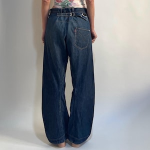 Könnte beinhalten: Ein Camisole-Top mit floralem Muster und Spaghettiträgern, kombiniert mit einer dunkelblauen Jeans mit weitem Bein. Die Jeans hat eine hohe Taille mit Gürteldetail und ein rotes Levi's-Etikett auf der Gesäßtasche. Das Outfit ist lässig und stilvoll.