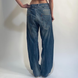 Könnte beinhalten: Ein rotes Crop-Top mit einem schwarz-weißen Design und eine blaue Jeans mit weitem Bein. Das Top hat einen quadratischen Ausschnitt und breite Träger. Die Jeans ist aus hellblauem Denim mit hoher Taille und lockerer Passform.