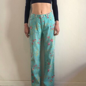 May include: A pair of light blue jeans with a floral print. The jeans have a straight leg and a mid-rise waist.