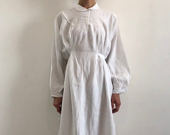 May include: A white linen dress with a peter pan collar and long sleeves. The dress has a gathered waist and a tie at the side.