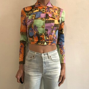 Könnte beinhalten: Eine kurze, mehrfarbige Satinjacke mit floralem und geometrischem Muster. Die Jacke hat einen Knopfschließe vorne und lange Ärmel.