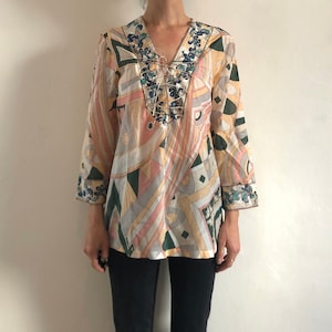 May include: A white, pink, and green patterned blouse with a lace-up neckline. The blouse has long sleeves and a relaxed fit.