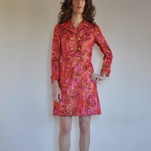 May include: A pink and orange floral print double-breasted coat with gold buttons. The coat is knee-length and has a fitted silhouette.