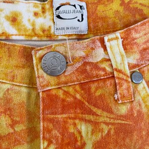 May include: Orange and yellow tie-dye denim jeans with a Cavalli Jeans label and a metal button with the Cavalli Jeans logo. The label reads "Cavalli Jeans" and "Made in Italy".