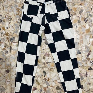 May include: High-waisted pants featuring a bold black and white checkered pattern. The garment includes two back pockets, a waistband with belt loops, and visible stitching along the seams, showcasing a classic straight-leg cut design.