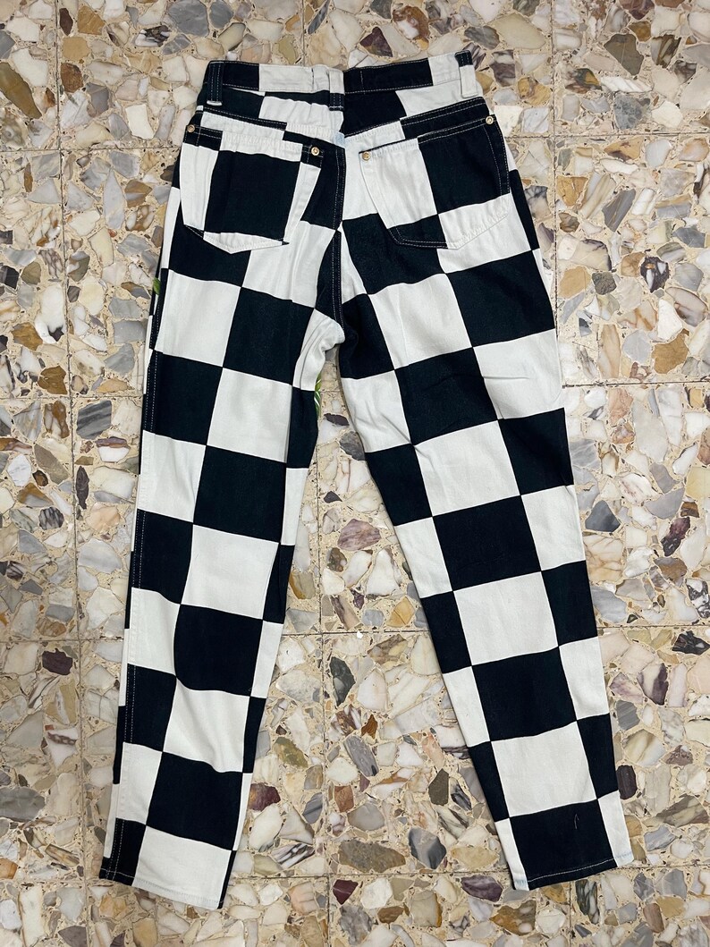 May include: High-waisted pants featuring a bold black and white checkered pattern. The garment includes two back pockets, a waistband with belt loops, and visible stitching along the seams, showcasing a classic straight-leg cut design.