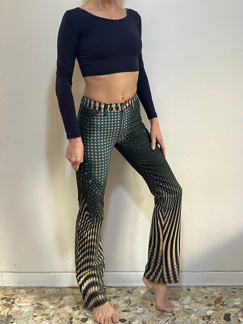 Puede incluir: Una persona que lleva un top negro de manga larga y pantalones estampados en negro y verde con un dise&ntilde;o geom&eacute;trico.
